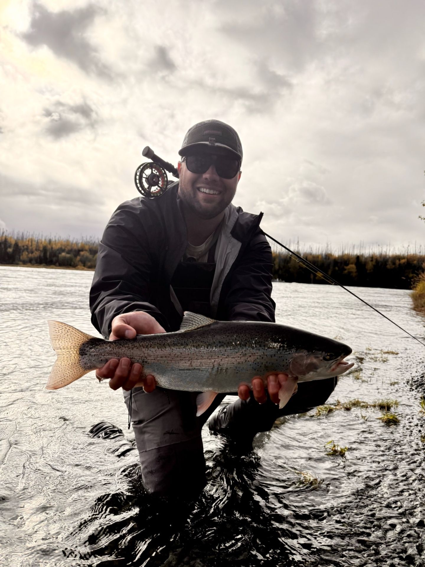 Angler wading in the river with a rainbow trout and fly rod